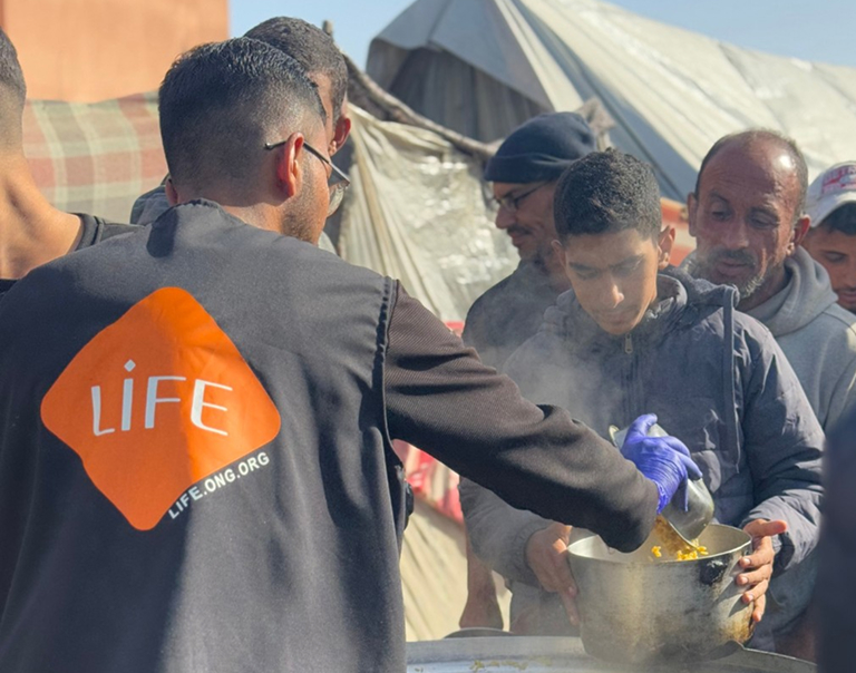 Un membre de l'équipe LIFE sert un repas chaud aux habitants d'un camp de déplacés.